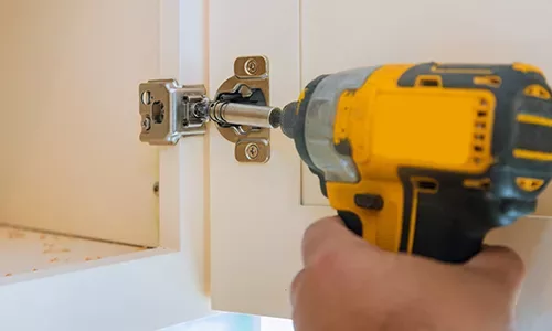 Carpentry assembly of furniture accessories in the kitchen door with a screwdriver a hinge to a kitchen cabinet.