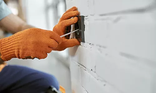 Close up of young man in work gloves fixing power electric socket with screwdriver